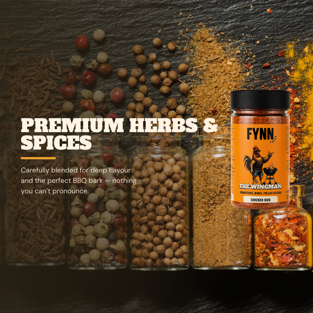 A promotional product shot for Fynn The Wingman premium herbs and spices, showing a jar of chicken rub alongside several glass jars of whole and ground spices, with loose spices scattered on a dark textured background and marketing text on the left.